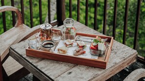A wooden table with a tray of food and drinks on a balcony with a view of palm trees. - LeRosa Valley Resort (Ubud)