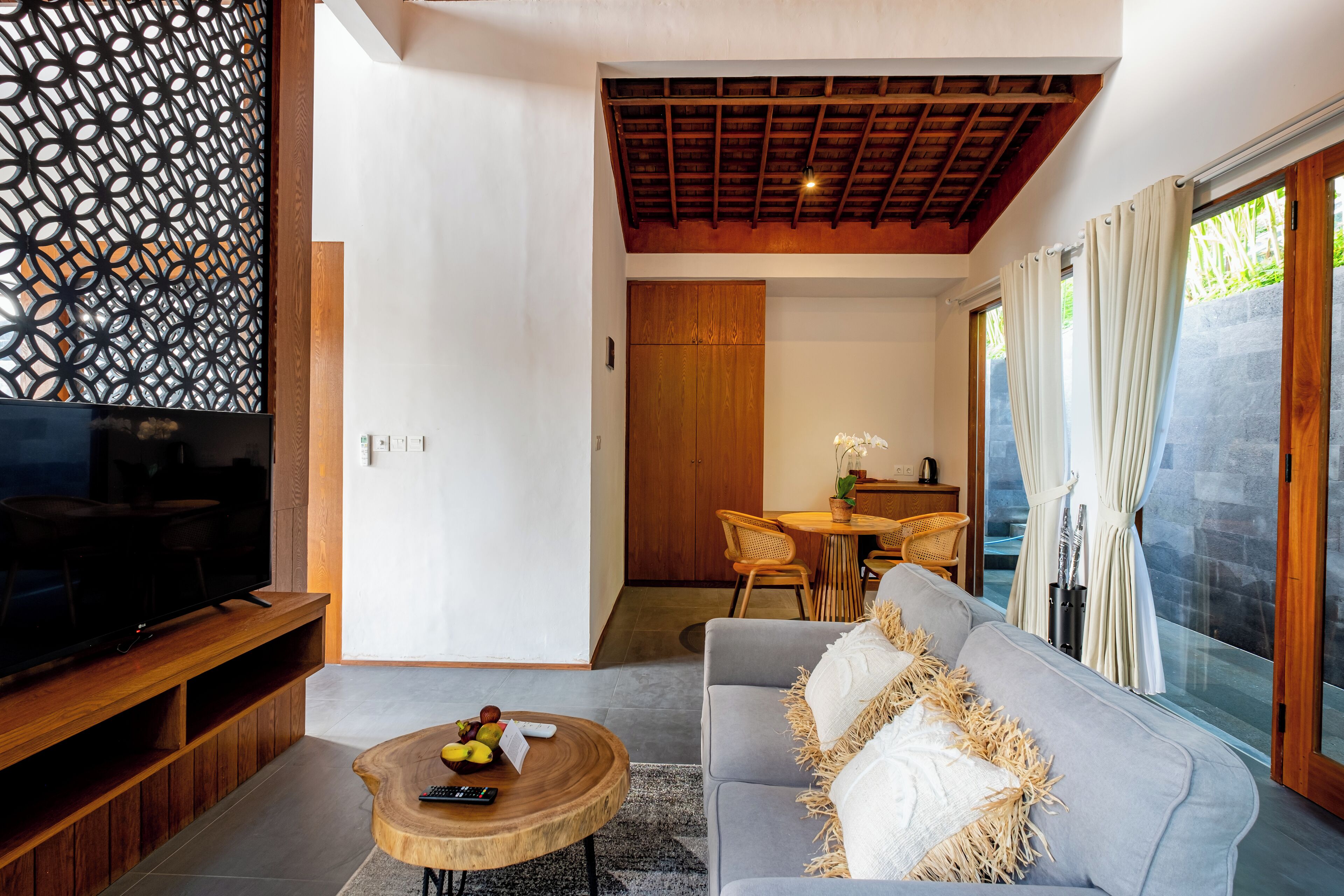 A modern living room with a TV, wooden coffee table, grey sofa, and a dining area with a table and chairs.