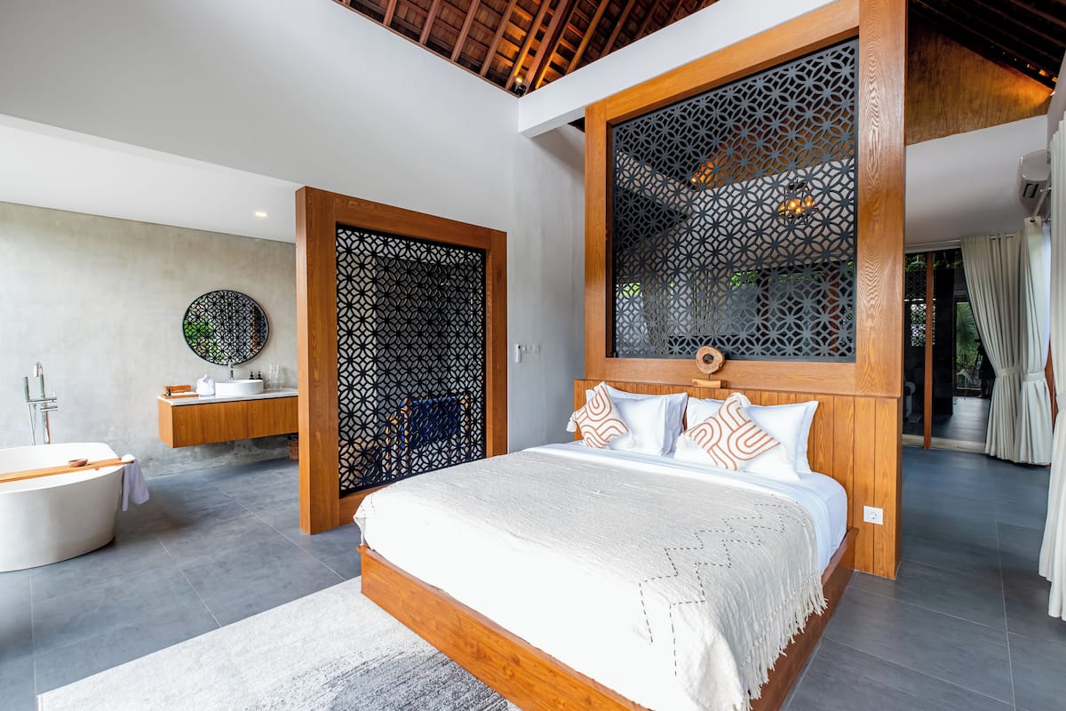 A modern bedroom with a large bed, wooden headboard, and a decorative screen.