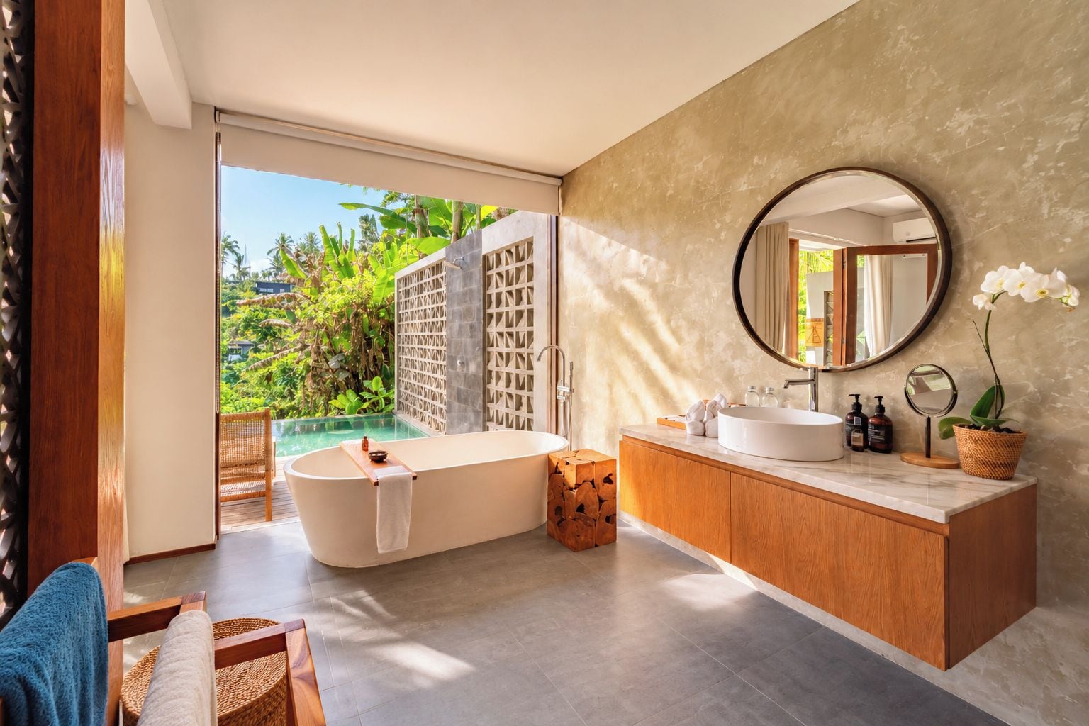 Un baño moderno con una bañera independiente, un espejo grande y vistas a un jardín exuberante.