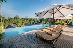 A wooden deck with lounge chairs and umbrellas overlooking a swimming pool, surrounded by lush greenery and palm trees. - LeRosa Valley Resort (Ubud)