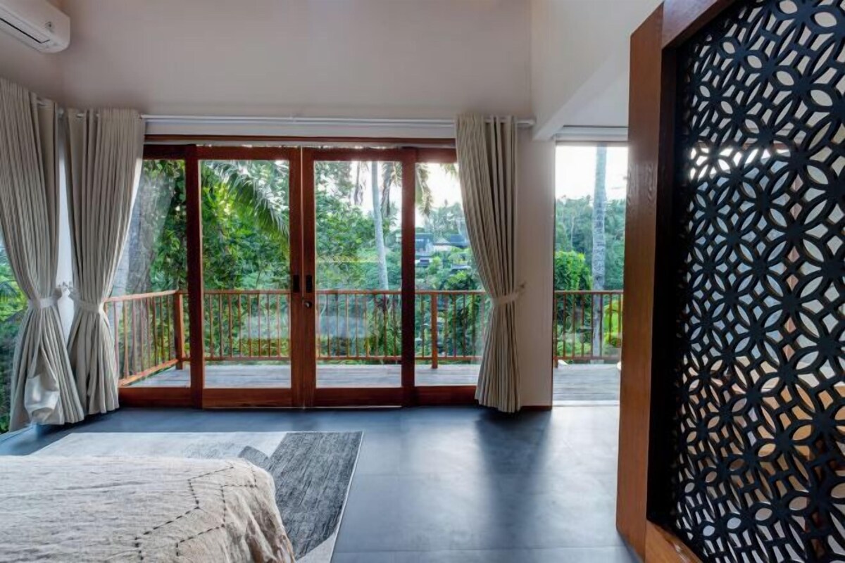 Un dormitorio con un amplio ventanal corredero que da a un balcón con vistas a la vegetación.