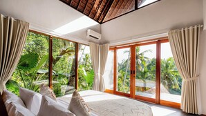 A bedroom with a large bed, curtains, and a view of lush greenery. - LeRosa Valley Resort (Ubud)