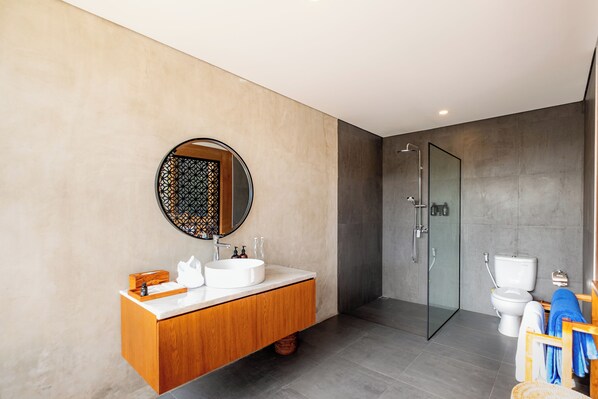 Un baño moderno con tocador de madera, espejo redondo, cabina de ducha de vidrio y un inodoro.