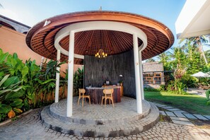 A circular outdoor seating area with a wooden ceiling and a central table, surrounded by lush greenery. - LeRosa Valley Resort (Ubud)