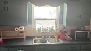 Eine Küche mit türkisfarbenen Schränken, einer Holzarbeitsplatte, einem Spülbecken, einem Fenster mit Blick auf die Straße und diversen Küchenutensilien.