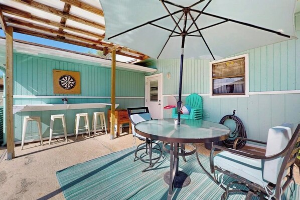 A covered patio with a table and chairs, a dartboard, and a window.