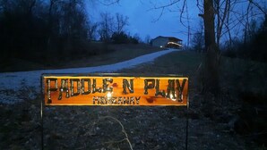 Une pancarte sur laquelle on peut lire « TADLE N PLAY », placée dans un cadre rural, avec un chemin de terre et des arbres.