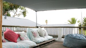 A covered outdoor seating area with a wooden deck, a cushioned bench with pillows, and a bean bag. - Cozy Crner, home away from home, mere 100m away from pristine beaches (Langebaan)