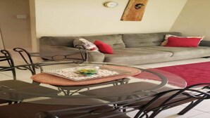 A dining area with a glass table and chairs, a woven placemat, and a grey sofa with red cushions in the background. - Jacaranda Vacation Home (Spanish Town)