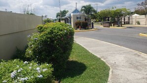 A residential street with a house featuring a blue roof and a small garden. - Jacaranda Vacation Home (Spanish Town)