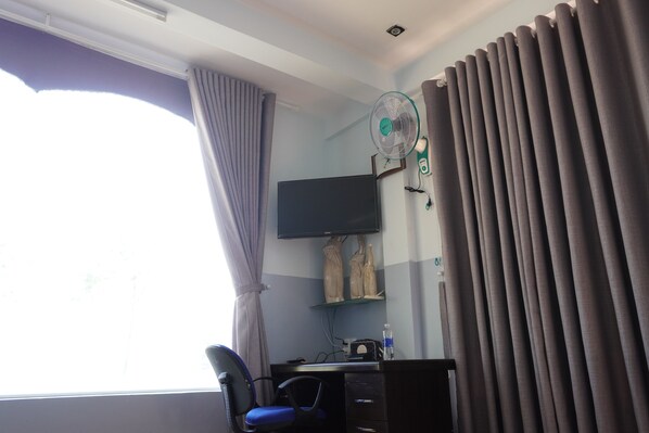 A hotel room with a desk, chair, TV, and curtains.