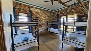 Une pièce avec des lits superposés, un mur en briques, un plancher en bois et un ventilateur de plafond.