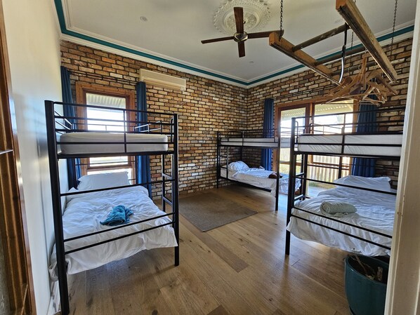 A room with bunk beds, a brick wall, wooden flooring, and a ceiling fan.