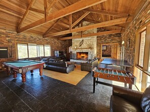 A spacious living area with a pool table, foosball table, and a stone fireplace.
