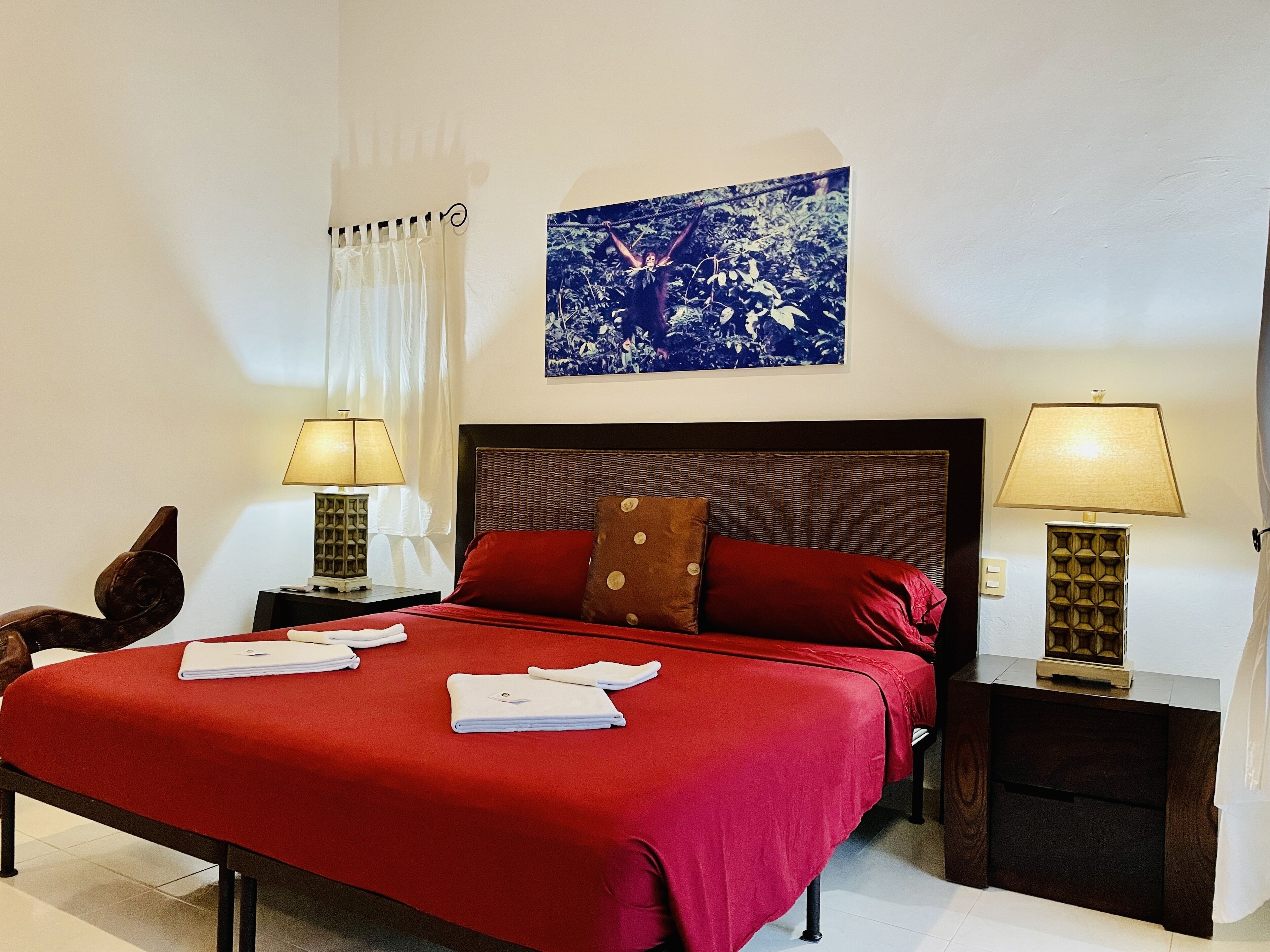A hotel room with a large bed, two bedside tables with lamps, a wall-mounted painting, and a window with curtains.