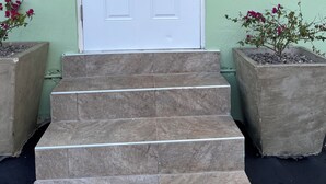 A white door with a security device, a set of stone steps leading up to the door, and two potted plants with pink flowers on either side. - The Hideaway cozy , centrally located apartment 3 minutes from town center (Mandeville)