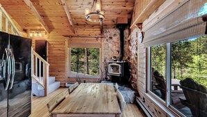 A wooden cabin interior with a stone wall, a wooden table, a black refrigerator, and a stone fireplace.