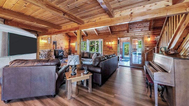 A log cabin interior with a living room, sofa, coffee table, fireplace, and a piano.
