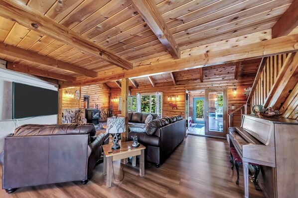 A log cabin interior with a living room, sofa, coffee table, fireplace, and a piano.