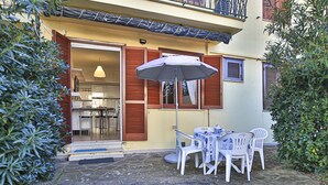 Un patio con una mesa y sillas bajo un toldo, una cocina visible a través de una puerta abierta, y suelo empedrado de piedra.