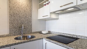 Una cocina moderna con encimeras de granito, un lavamanos de acero inoxidable, una placa de inducción negra, armarios blancos y un estante empotrado para especias.