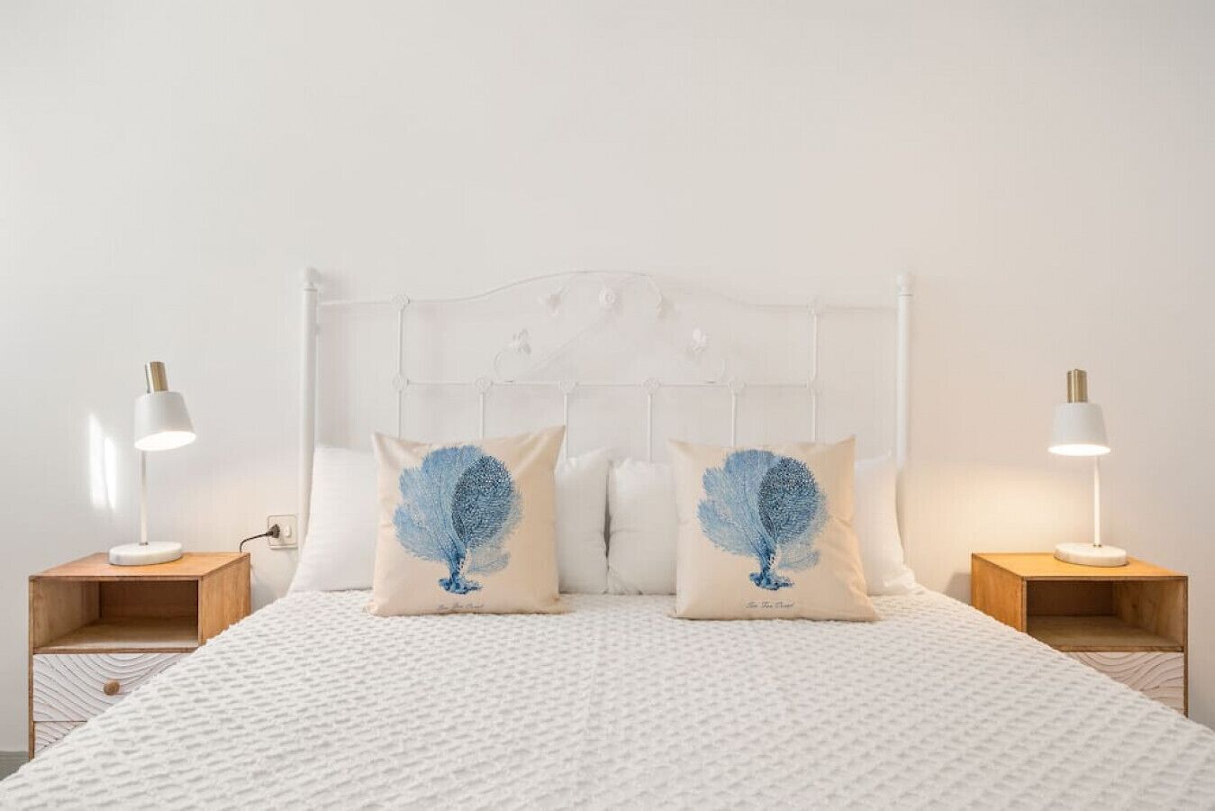 A neatly made bed with a white headboard, two bedside lamps, and two decorative pillows with a blue feather pattern.