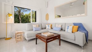 A modern living room with a sofa, coffee table, and a large window with a view of greenery. - Villa Calma a gift for your eyes (San Jaime Mediterráneo)