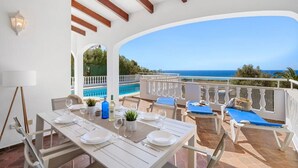 A dining area with a view of the sea, a pool, and outdoor seating. - Villa Calma a gift for your eyes (San Jaime Mediterráneo)