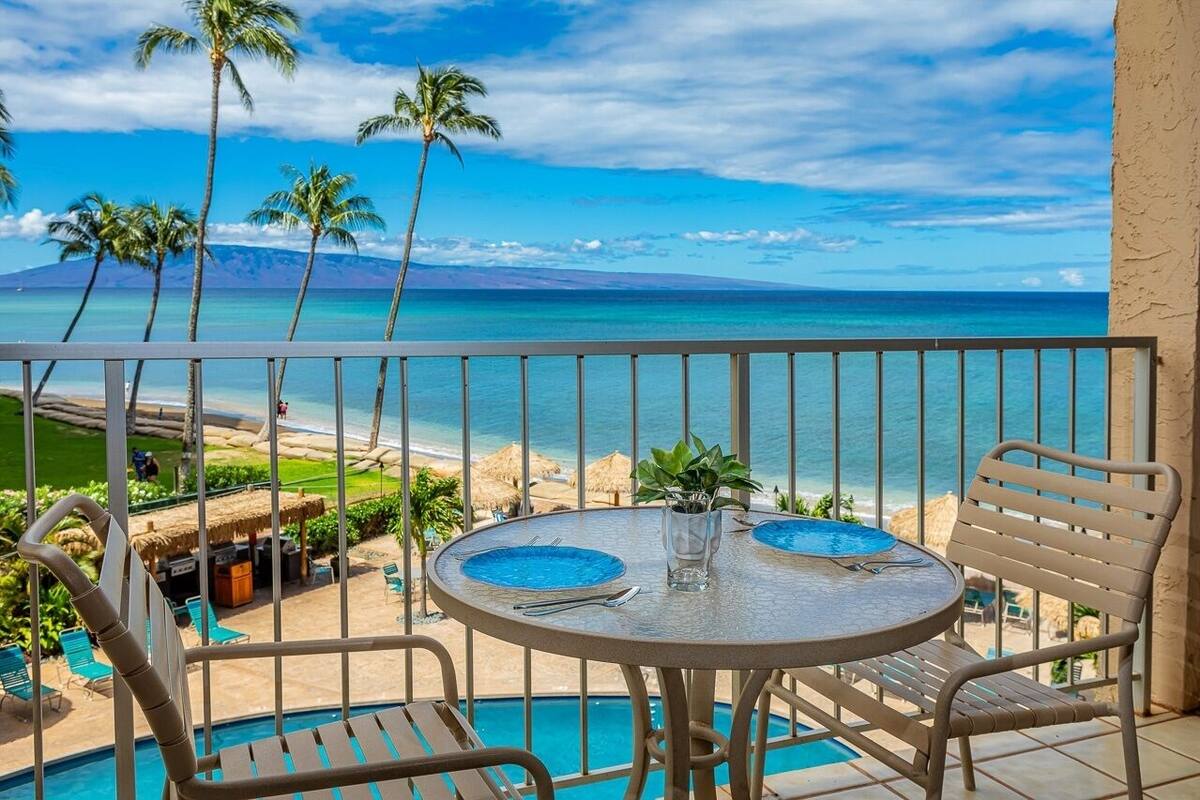 Ein Balkon mit Tisch und Stühlen mit Blick auf einen Strand und den Ozean.