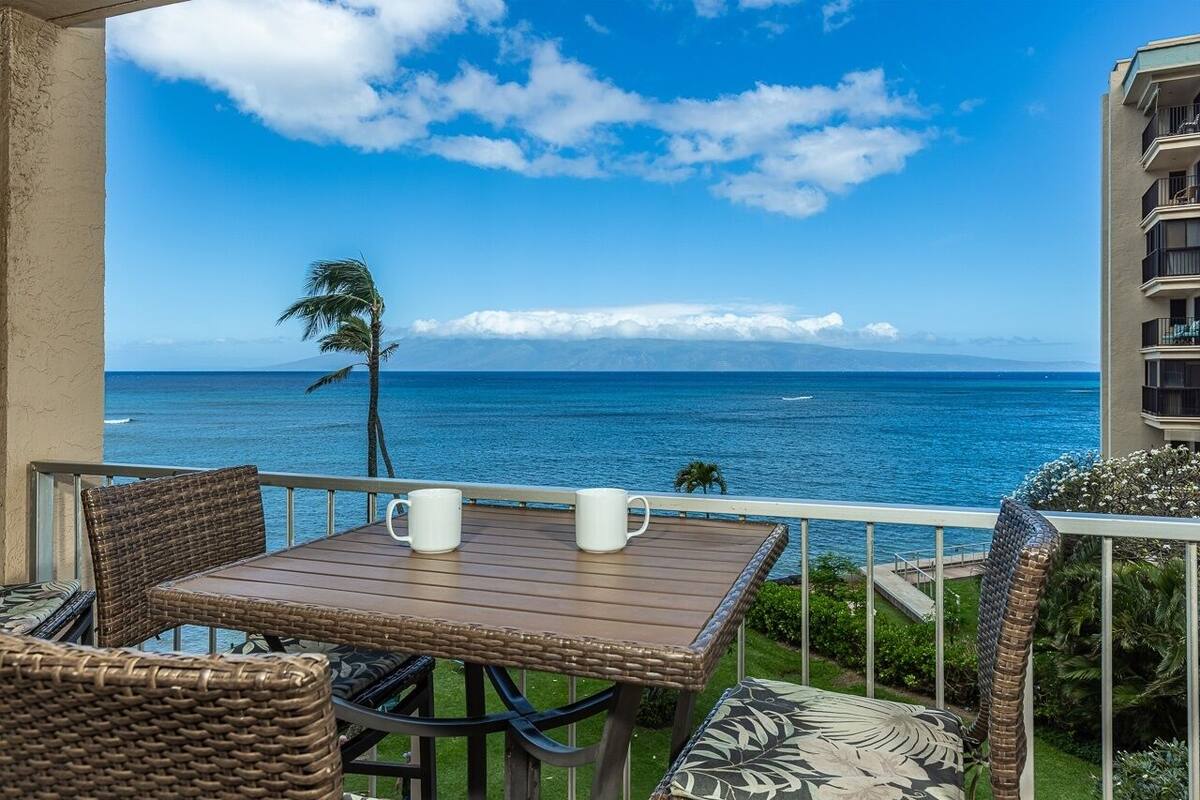 Ein Balkon mit Korbmöbeln, zwei weiße Tassen und Blick aufs Meer.