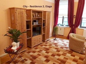Uma sala de estar com um armário de madeira, um sofá, uma planta em vaso e piso de azulejos.