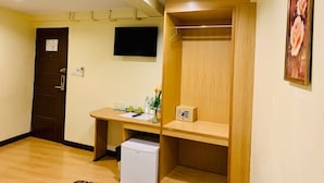 Una habitación con un escritorio de madera, un refrigerador pequeño, un televisor montado en la pared y un armario de madera.