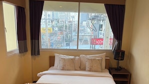 Una habitación de hotel con una cama, una ventana con cortinas, una mesita de noche y un sofá con cojines decorativos.