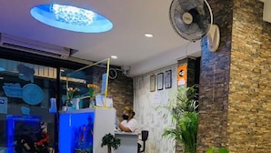 Un hall de hotel con mostrador de recepción, una mesa de vidrio y un ventilador grande.