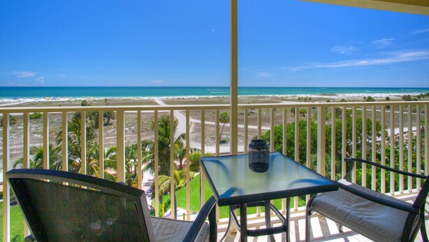 Un balcon avec une table et des chaises en verre donnant sur une plage.