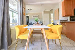 Ein Essbereich mit einem weißen Tisch und vier gelben Stühlen, eine Küche mit Holzschränken und im Hintergrund ein Blick auf das Wohnzimmer.