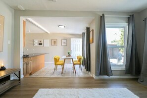 Eine moderne Küche mit integrierter Kücheninsel, einem Essbereich mit gelben Stühlen und einem großen Fenster mit grauen Vorhängen.