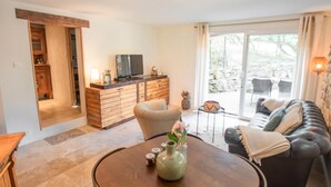 Un salon comprenant un canapé, une table basse et un téléviseur. Une porte-fenêtre coulissante donne accès à un espace extérieur.
