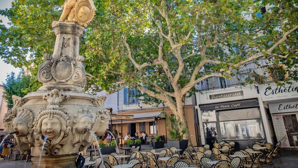 Une place publique agrémentée d’une fontaine décorative, de sièges extérieurs et de cafés.
