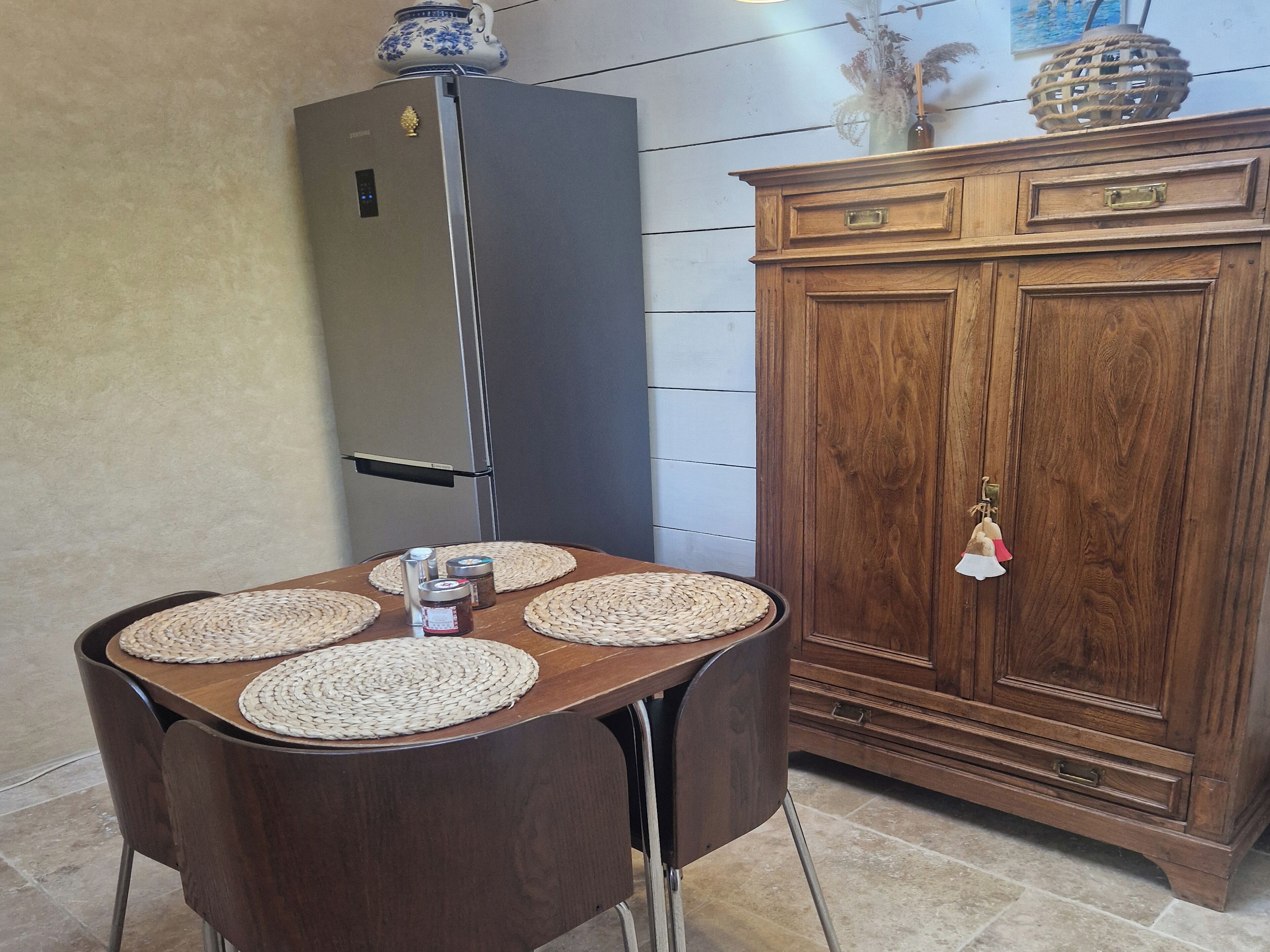 A dining area with a table set for four, a refrigerator, and a wooden cabinet with drawers.