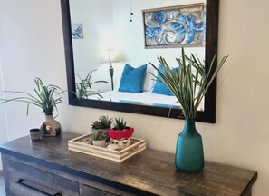 A wooden dresser with a mirror above it, reflecting a bed with blue bedding. There are potted plants on the dresser. - Condo with View of El Malecón (Puerto Peñasco)
