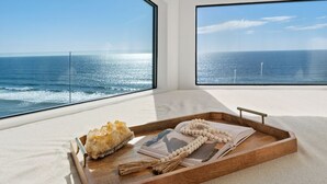 Ein Zimmer mit einem großen Fenster mit Blick auf den Ozean, ein Holztablett mit einem Kristall, einer Perlenkette und einem Buch.