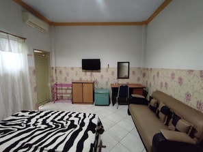 Ein Zimmer mit einem Bett, einem Sofa, einem Schreibtisch, einem Fernseher und einem Spiegel.