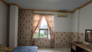 Une chambre à coucher comprenant un lit, un bureau, une fenêtre avec des rideaux et un climatiseur fixé au mur.