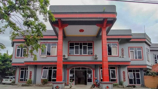 Un bâtiment à deux étages, doté d’une façade rouge et grise, avec une entrée centrale surmontée d’une arche rouge et de nombreuses fenêtres.