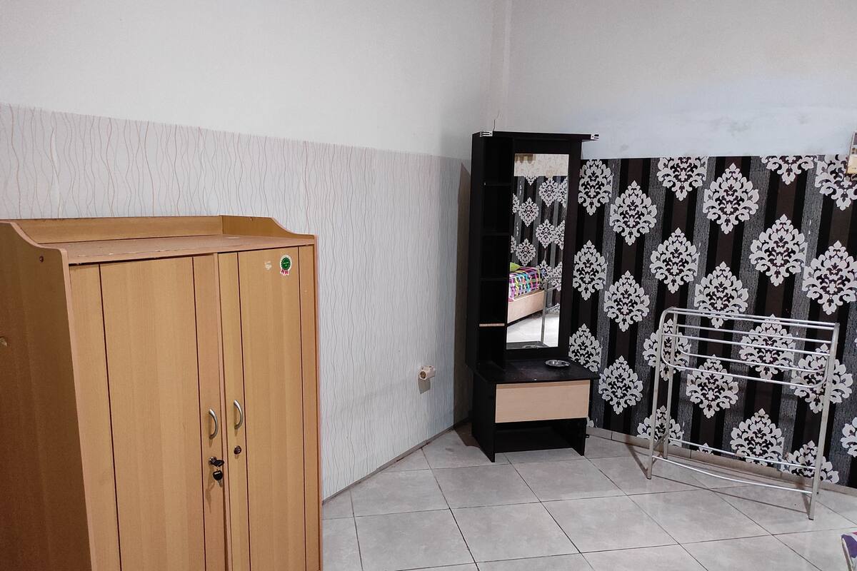 A room with a wooden wardrobe, a black cabinet with a mirror, and a patterned wall.
