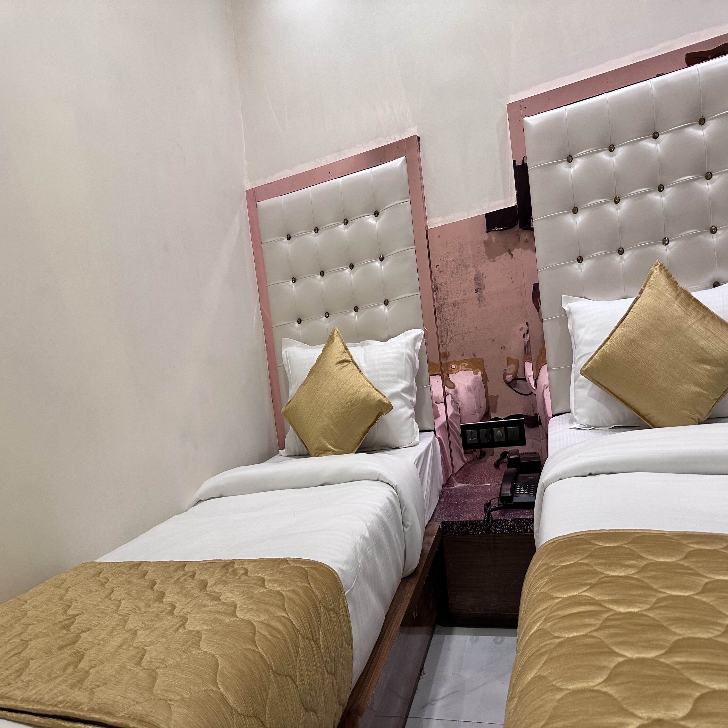 Habitación de hotel con dos camas, cada una con cabecero, ropa de cama blanca y almohada decorativa dorada.