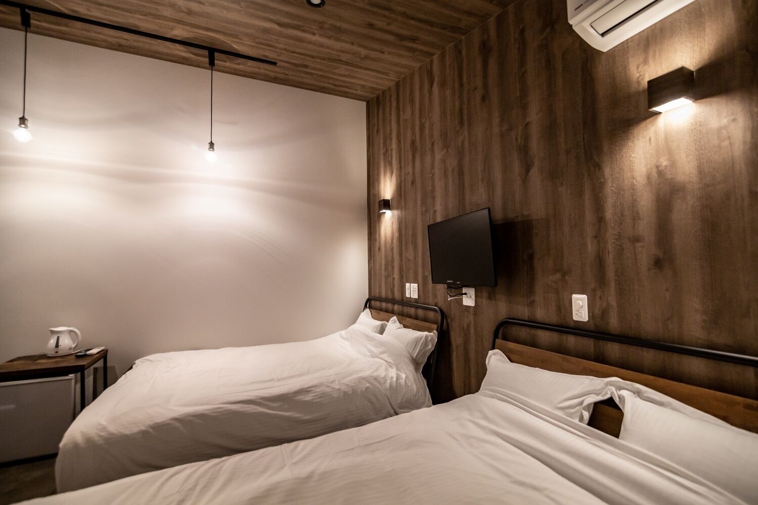 A hotel room with two beds, a TV mounted on the wall, and a small table with a kettle.