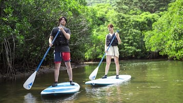 Two people stand-up paddleboarding on a calm river surrounded by dense greenery.